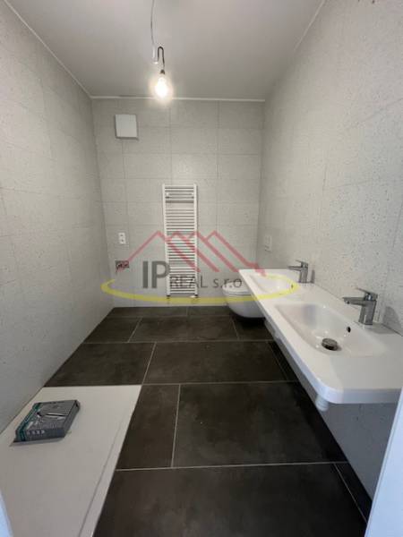 Fürdőszoba egy kétszobás lakásban sötét padlólappal és létra radiátorral.