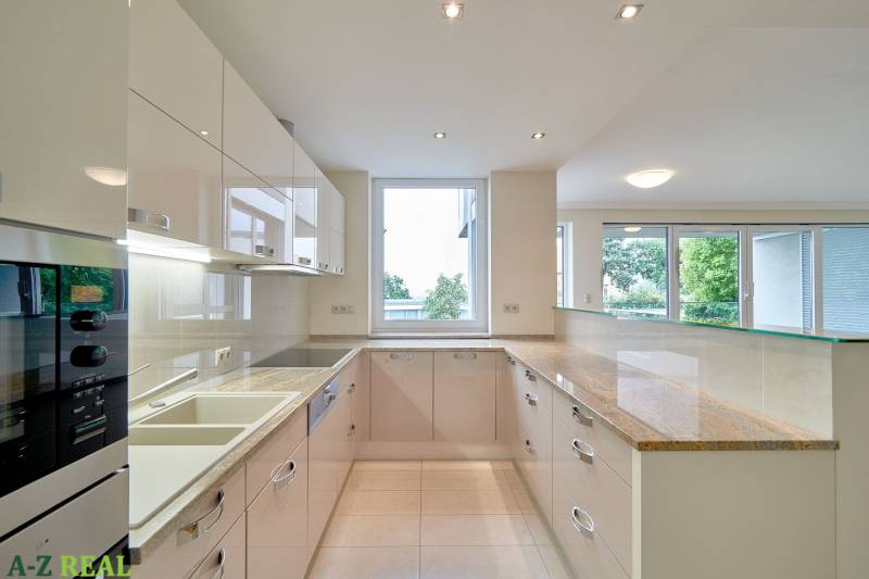 Konyha egy háromszobás lakásban nagy ablakkal, fehér szekrényekkel és fényes munkalappal.