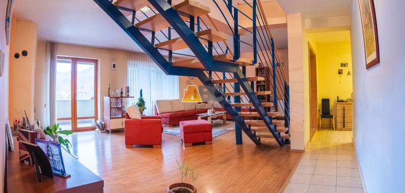 Egy villa belső tere fa dekorációjú padlóval, lépcsővel és piros ülőgarnitúrával.