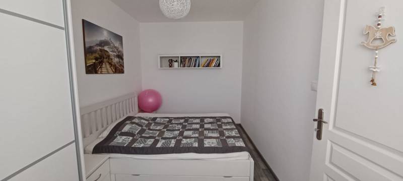 Hálószoba ággyal, képpel, könyvekkel és fa dekorációjú padlóval egy háromszobás lakásban.