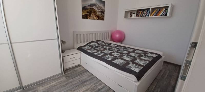 Hálószoba egy háromszobás lakásban gardróbbal, ággyal, könyvekkel és fa dekorációjú padlóval.