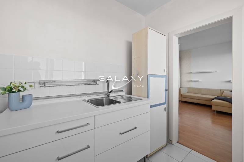 Konyha egy egyszobás lakásban fehér konyhaszekrényekkel és kilátással a nappalira.