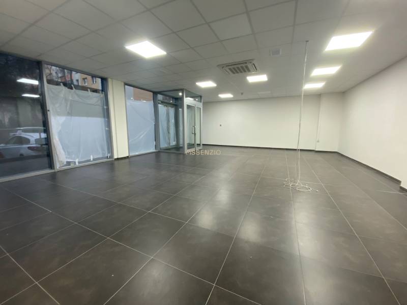 Kereskedelmi helyiségek sötét csempékkel, fehér falakkal és üveg kirakatokkal.