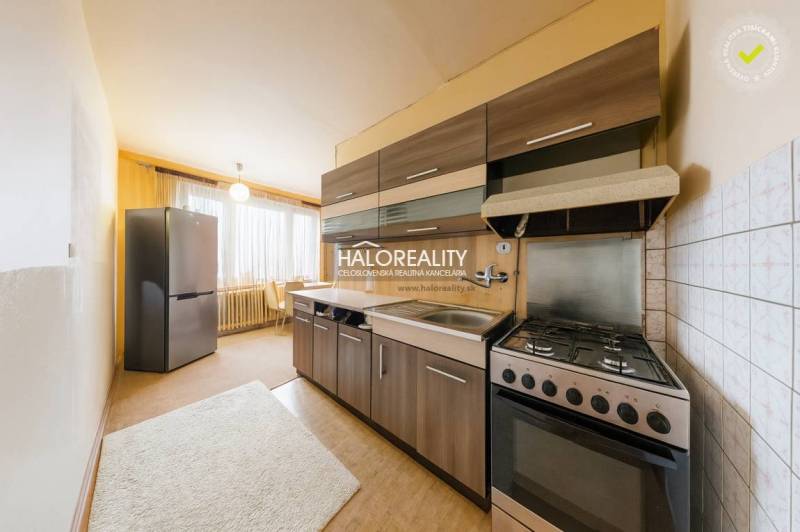 A háromszobás lakás konyhája sötét szekrényekkel, világos falakkal és nagy ablakkal.