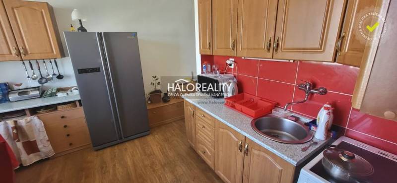 Konyha egy egyszobás lakásban fa szekrényekkel, piros csempékkel és nagy hűtőszekrénnyel.