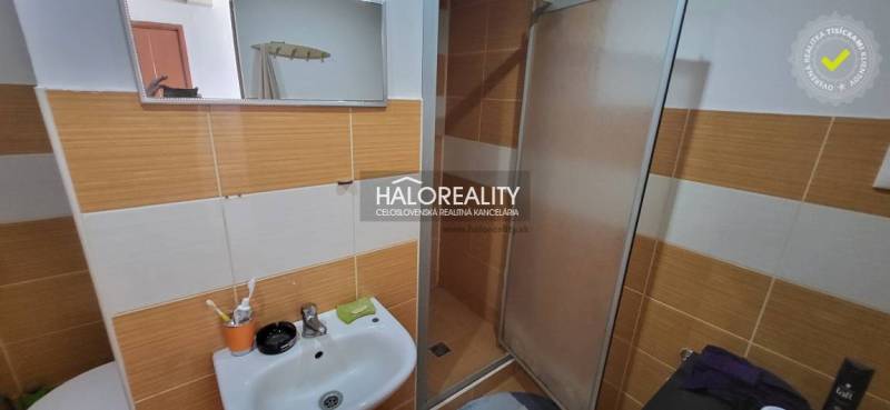 Fürdőszoba mosdóval és zuhanyzóval egy egyszobás lakásban, narancssárga-fehér csempékkel.