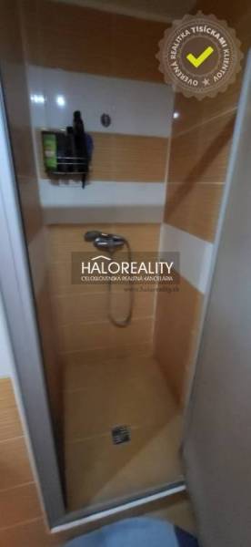 Zuhanykabin egy egyszobás lakásban narancssárga csempékkel és fali tárolóval.