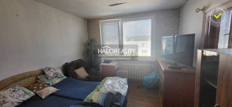 Szoba egy egyszobás lakásban ággyal, székkel, televízióval és nagy ablakkal.