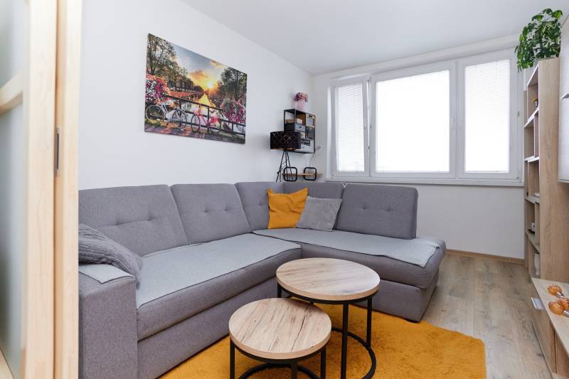 Nappali egy kétszobás lakásban sarokkanapéval, fa dekorációjú padlóval és ablakkal.