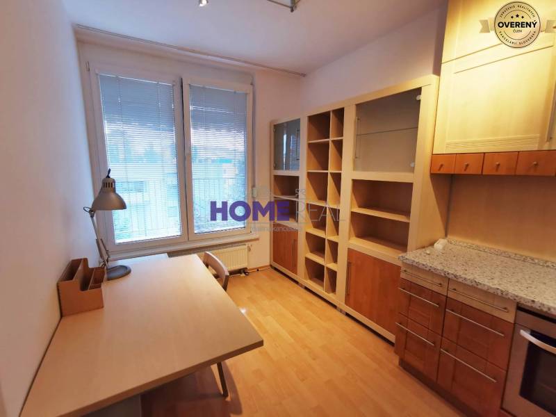 Dolgozószoba egy kétszobás lakásban, fa mintázatú padlóval, asztallal és könyvespolccal.