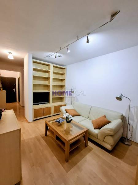 Nappali egy kétszobás lakásban krémszínű kanapéval és fa mintázatú padlóval.