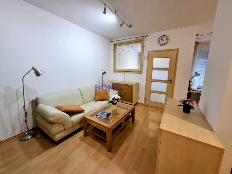 Nappali egy kétszobás lakásban kanapéval, lámpával és fa dekor padlóval.