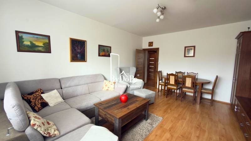 Nappali egy háromszobás lakásban sarokkanapéval és fa mintázatú padlóval.