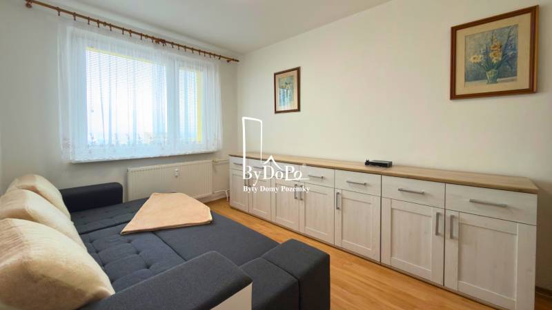 Szoba kanapéval, bútorokkal és fa dekorációjú padlóval egy háromszobás lakásban.