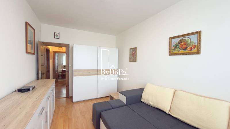 Nappali kanapéval, szekrénnyel és fa mintázatú padlóval egy háromszobás lakásban.