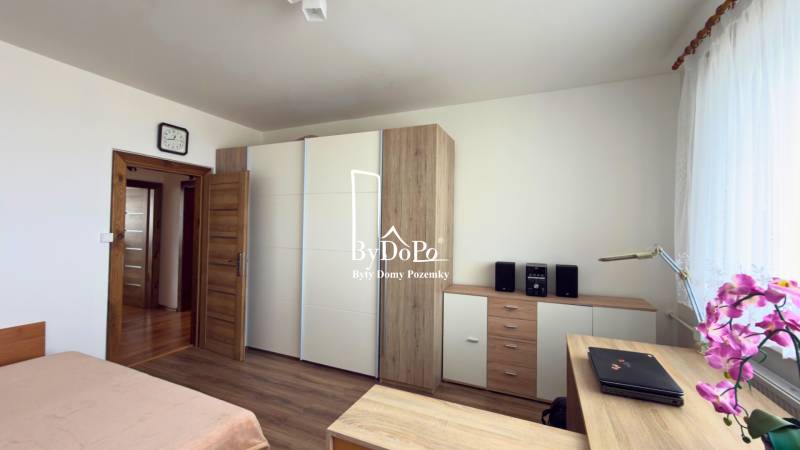 Hálószoba fa mintás padlóval, beépített szekrény és növény a háromszobás lakásban.