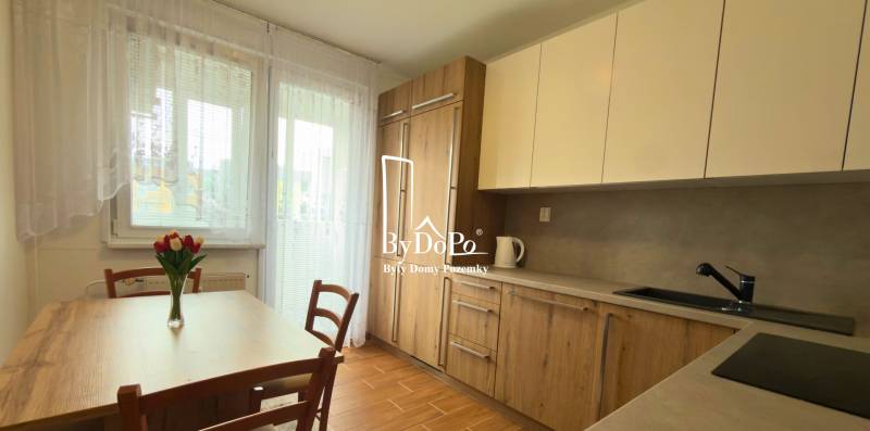 Konyha egy háromszobás lakásban fa dekorációval és világos bútorokkal, elegáns virágok az asztalon.