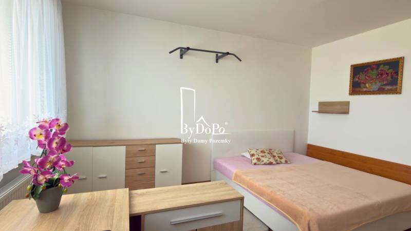 Hálószoba ággyal, szekrénnyel és dekoratív virágokkal egy háromszobás lakásban.