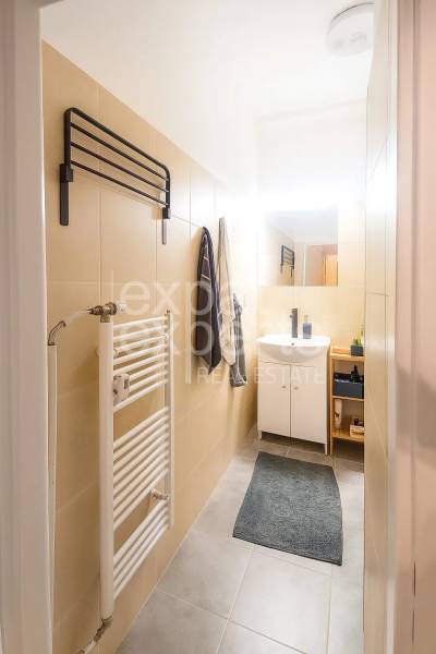Fürdőszoba egy háromszobás lakásban világos csempékkel, mosdóval és létraszerű radiátorral.