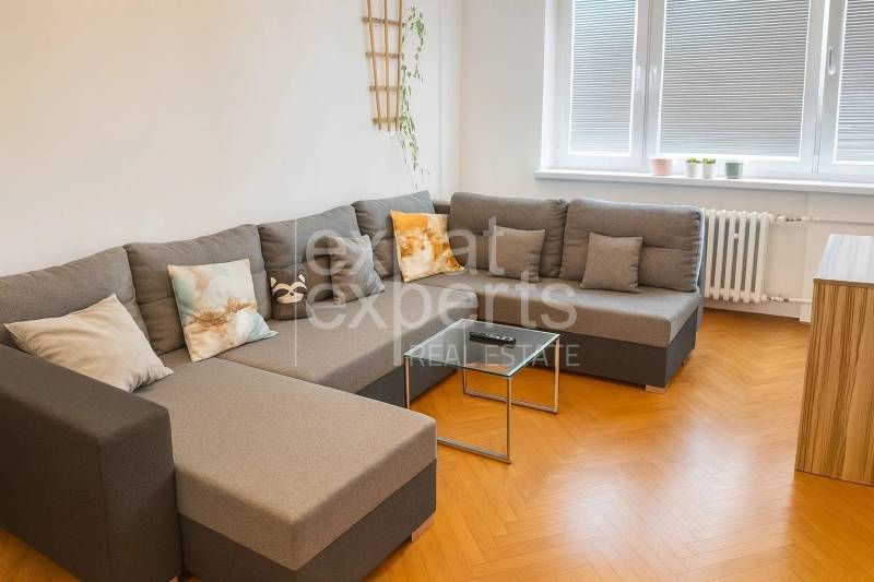 Nappali kényelmes kanapéval és fa mintázatú padlóval egy háromszobás lakásban.