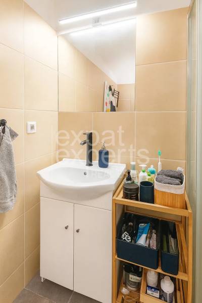 Fürdőszoba mosdóval, tárolóhellyel és világos csempével egy háromszobás lakásban.
