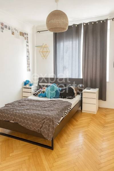 Hálószoba ággyal, éjjeliszekrényekkel és fa dekorációjú padlóval egy háromszobás lakásban.