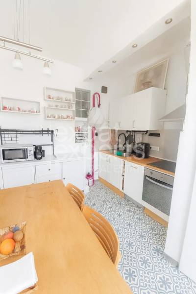 Konyha egy háromszobás lakásban étkezőasztallal, mintás padlóval és fehér szekrényekkel.