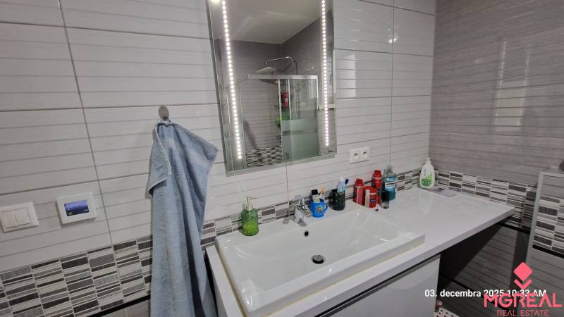 Fürdőszoba családi házban mosdóval, világítással ellátott tükörrel és zuhanyzóval.