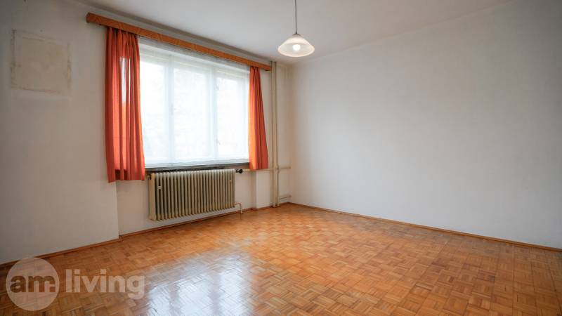 Szoba fa mintázatú padlóval, fehér falakkal és narancssárga függönyökkel egy családi házban.