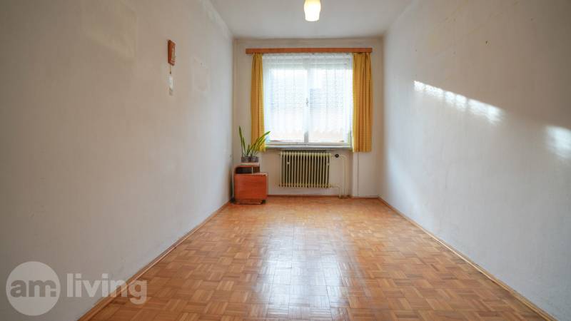 Szoba egy családi házban, fa dekoros padlóval, radiátorral és függönyös ablakkal.