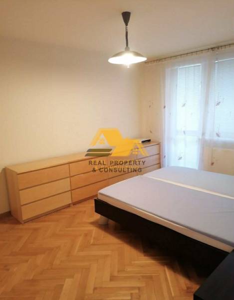 Hálószoba egy háromszobás lakásban, ággyal és komóddal, fa dekorációjú padlón.