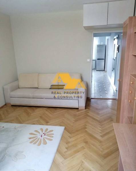 Nappali egy háromszobás lakásban fa dekor padlóval és világos kanapéval.