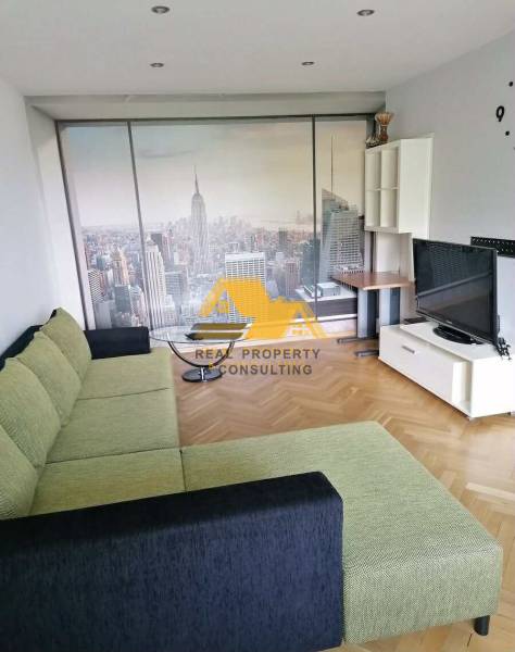 Nappali babapiskóta színű kanapéval, New York tapétával és fa dekor padlóval egy háromszobás lakásban.