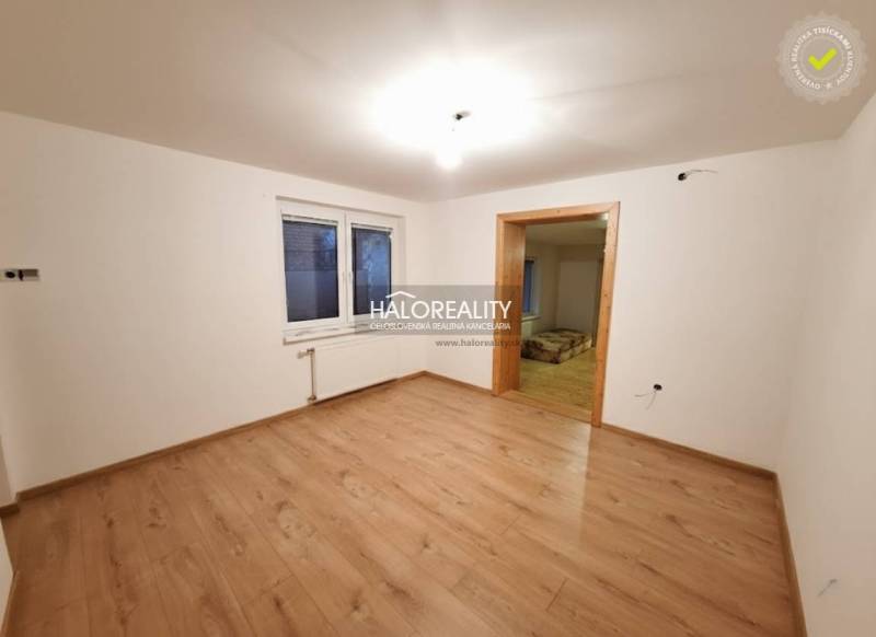 Egy családi ház szobája fa mintázatú padlóval és fehér falakkal.