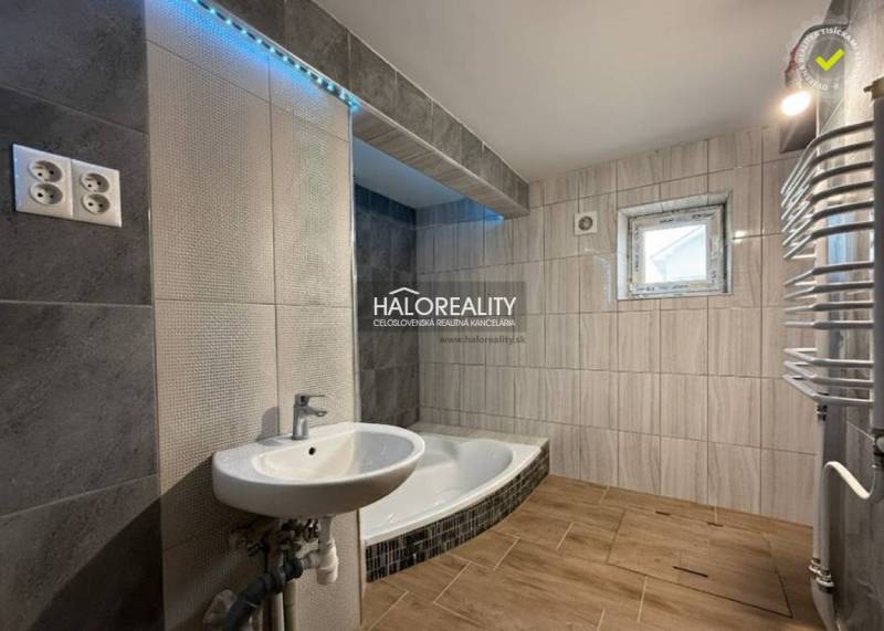 Családi ház fürdőszobája káddal, mosdóval és fa dekoros padlóval.