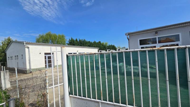 A fehér épület a Skladov és hálok része, kerítéssel és növényzettel körülvéve.