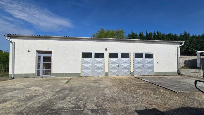 Fehér épület négy fémkapuval és bejárattal Selyén, raktárak és csarnokok számára alkalmas.