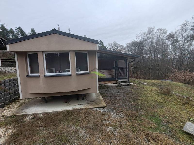 A Fő utcán található ház Újkelcsén, fákkal körülvéve és enyhén lejtős terepen.