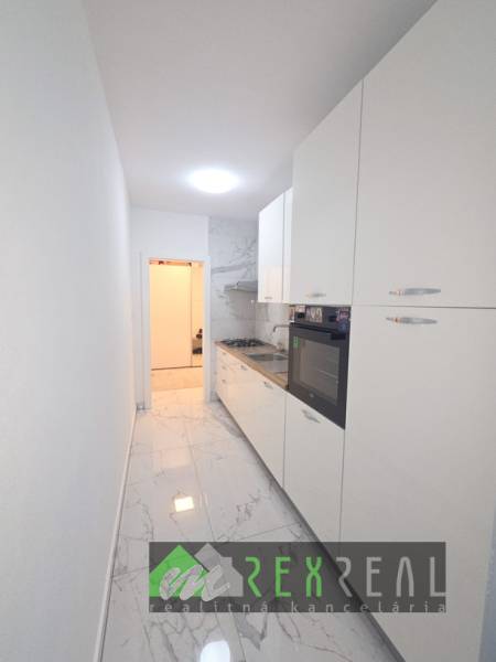 Keskeny fehér konyha főzőlappal és sütővel, márvány mintás padlóval egy háromszobás lakásban.