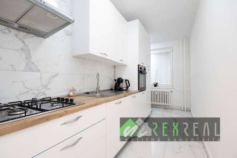 Konyha fehér szekrényekkel, márvány padlóval és beépített készülékekkel egy háromszobás lakásban.