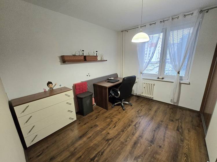 Dolgozószoba egy háromszobás lakásban fa hatású padlóval, asztallal és székkel.