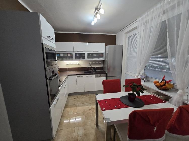 Konyha egy háromszobás lakásban fényes fehér szekrényekkel, készülékekkel és étkezőasztallal.