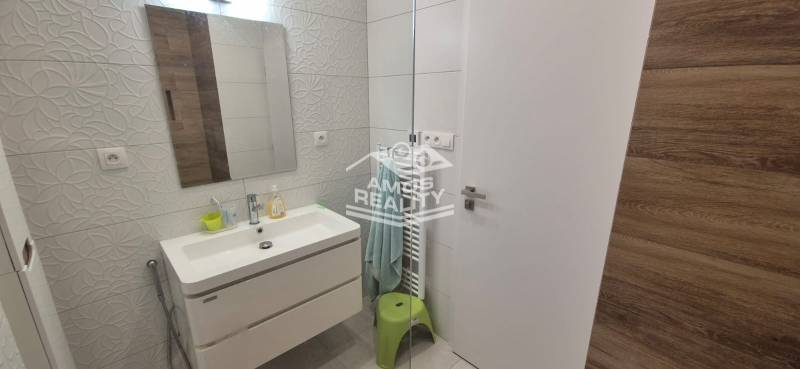 Fürdőszoba családi házban mosdóval, dombornyomott csempékkel, tükörrel és megvilágított falakkal.