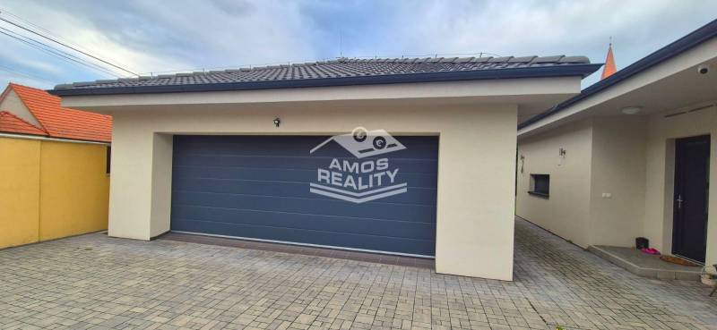 Garázs térkővel a családi ház mellett Studienkában, kőburkolattal és szürke kapuval.