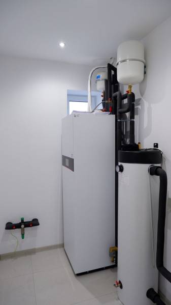 A családi ház fürdőszobájának berendezése bojlerekkel és csövekkel, világos falakkal.