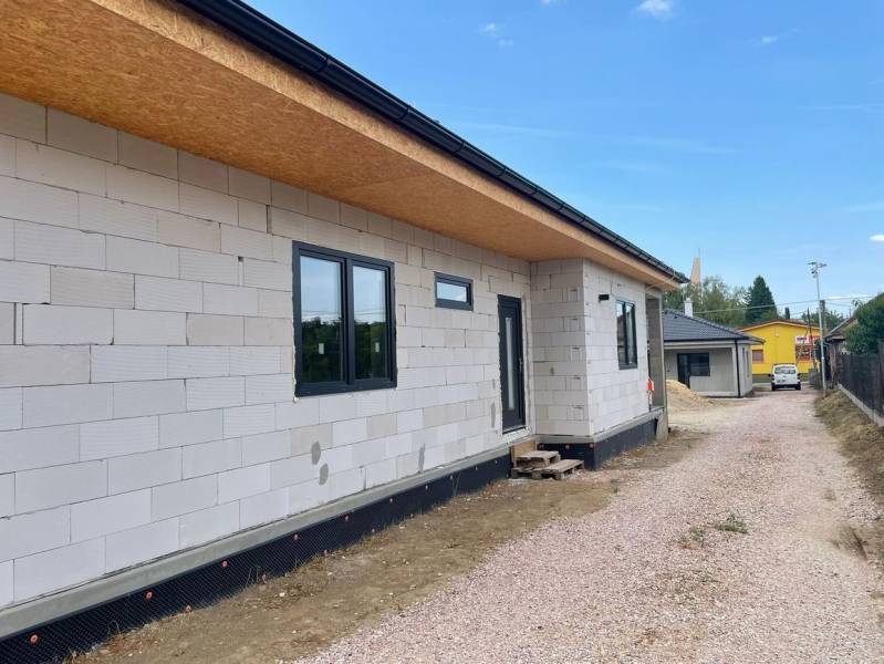 Egy családi ház Radaván építés alatt, szigetelés nélküli homlokzattal és kavicsos úttal.