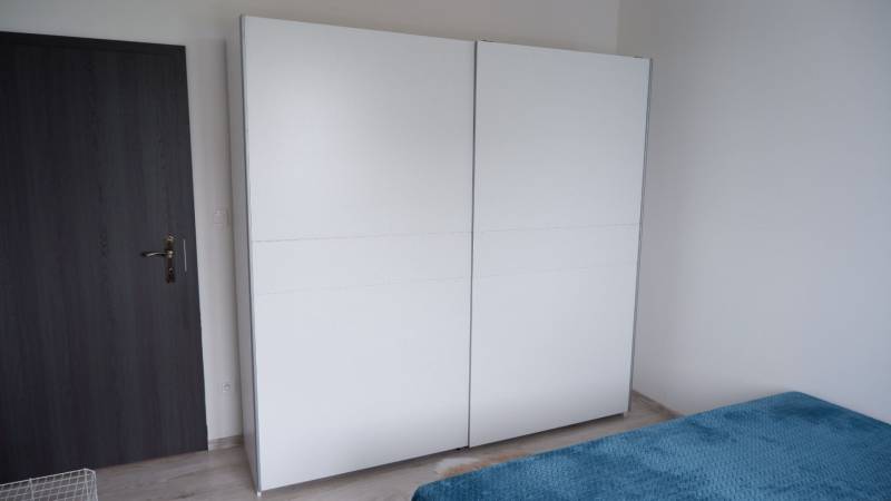 Fehér szekrény és ágy kék takaróval egy családi ház belső terében.