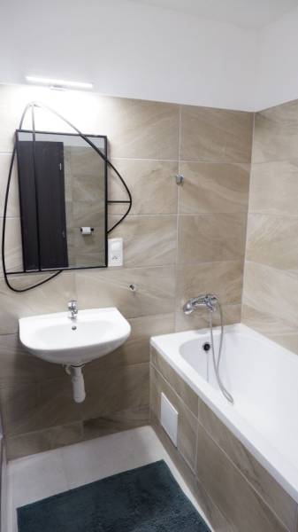 Fürdőszoba káddal, mosdóval és tükörrel, homokszínű csempékkel.