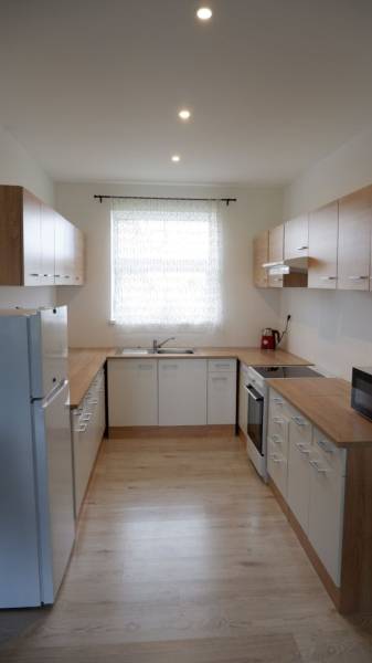 Konyha családi házban fehér szekrényekkel és fa dekoros padlóval.