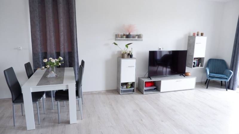 Családi ház belső tere étkezőasztallal, televízióval és fa dekorációjú padlóval.